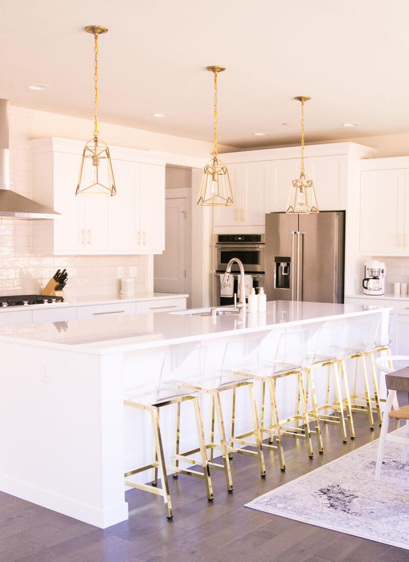 White and gold kitchen, gold lantern pendant lights, acrylic bar stools with gold legs