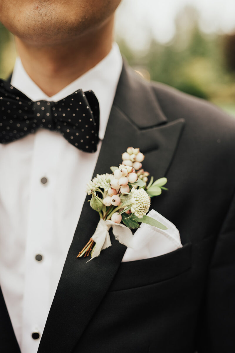 Seattle wedding, groom boutonniere with berries, groom getting ready photos, wedding outfit for groom, groom wearing polka dot bow tie, The Black Tux peak lapel tuxedo, outdoor wedding