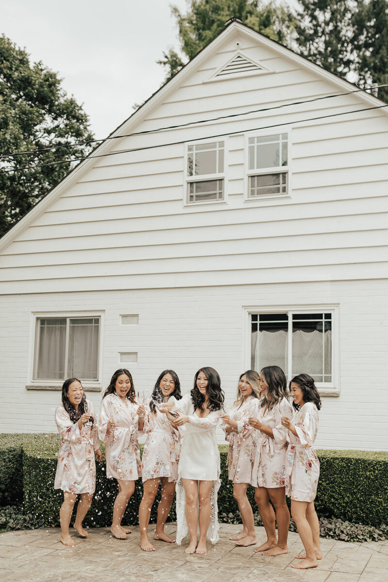Seattle outdoor wedding at Rock Creek Gardens, wedding getting ready photos wearing floral robes from BHDLN and popping champagne, mauve floral robes, bridal white lace robe with silk chemise, wedding outfits, wedding blogger