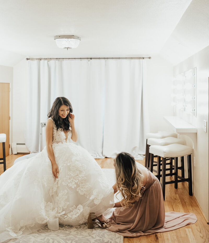 Seattle wedding, wedding outfits, wedding getting ready photos with bride and and Matron of Honor putting on her shoes, Calla Blanche Willow dress, wedding dress with dramatic long train