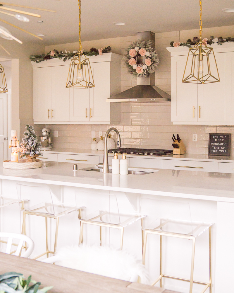 White and gold kitchen with Christmas decor, clear bar stools, wreaths and garland in kitchen, subway tile, gold pendant lights