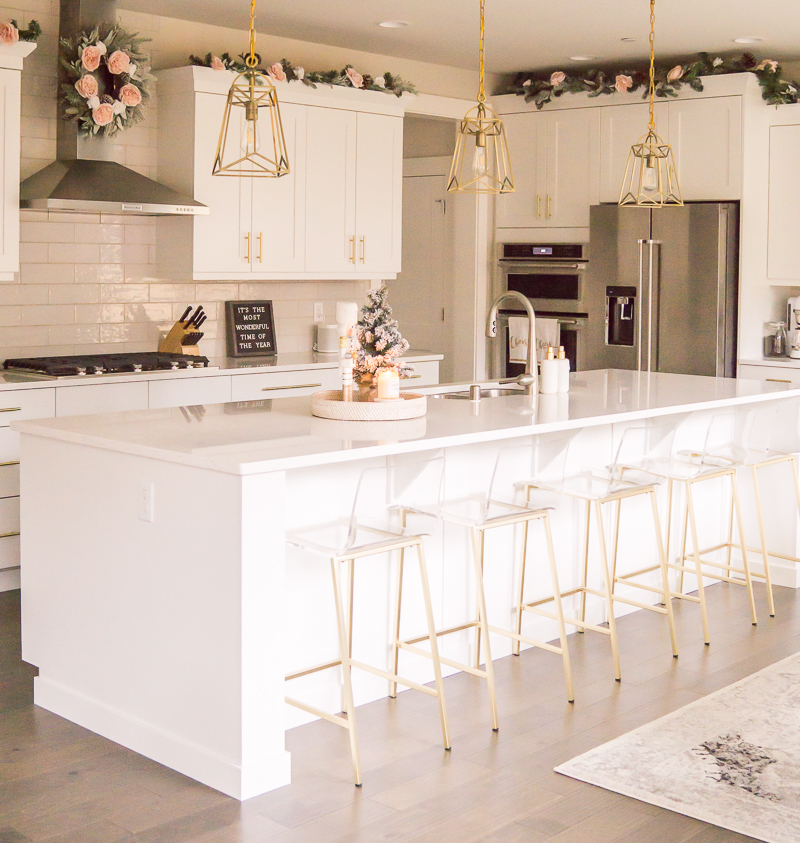 White and gold kitchen with Christmas decor, clear bar stools, wreaths and garland in kitchen, subway tile, gold pendant lights