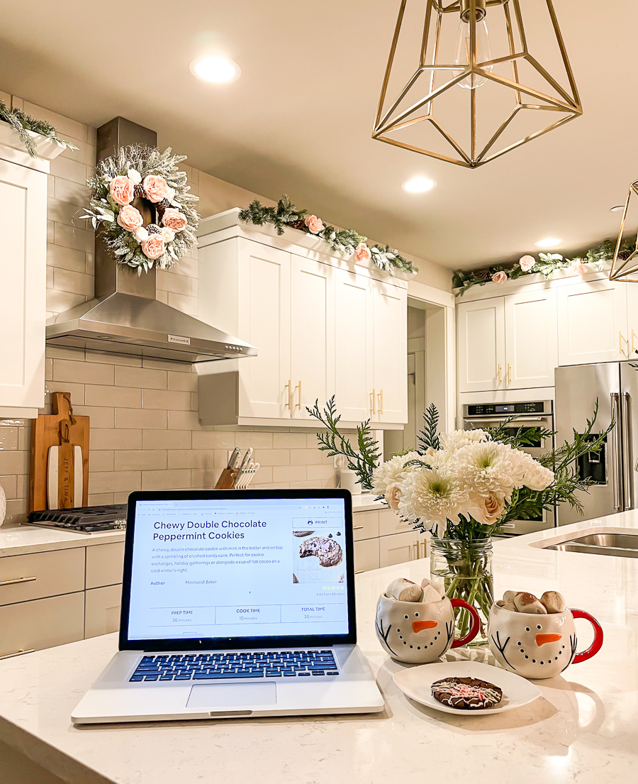 10 VIRTUAL HOLIDAY PARTY IDEAS FOR THE WHOLE FAMILY - Try a recipe together, white kitchen, Christmas kitchen, flocked wreath on kitchen hood, garland on kitchen cabinets