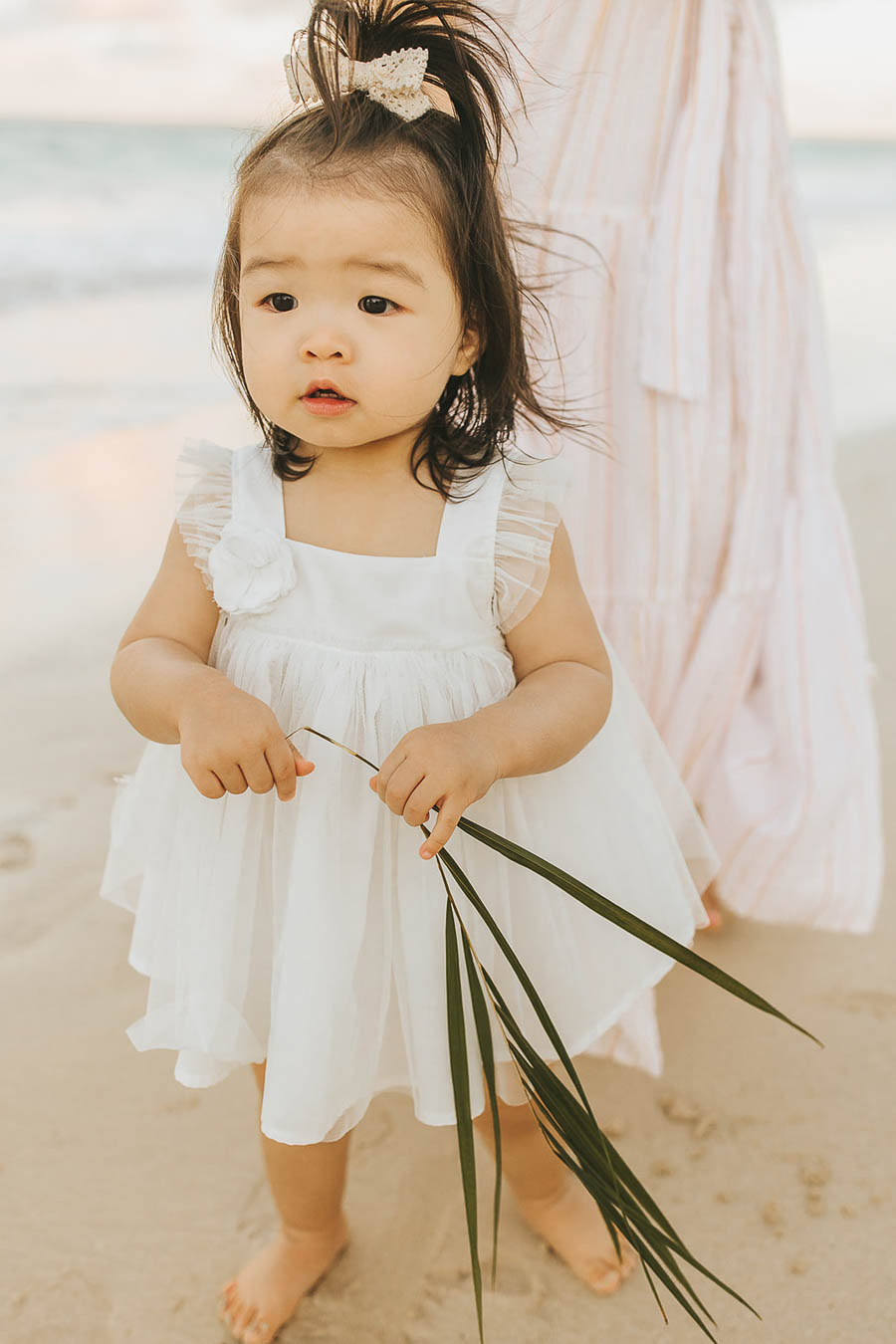 Toddler girl in white tulle dress on the beach with bow