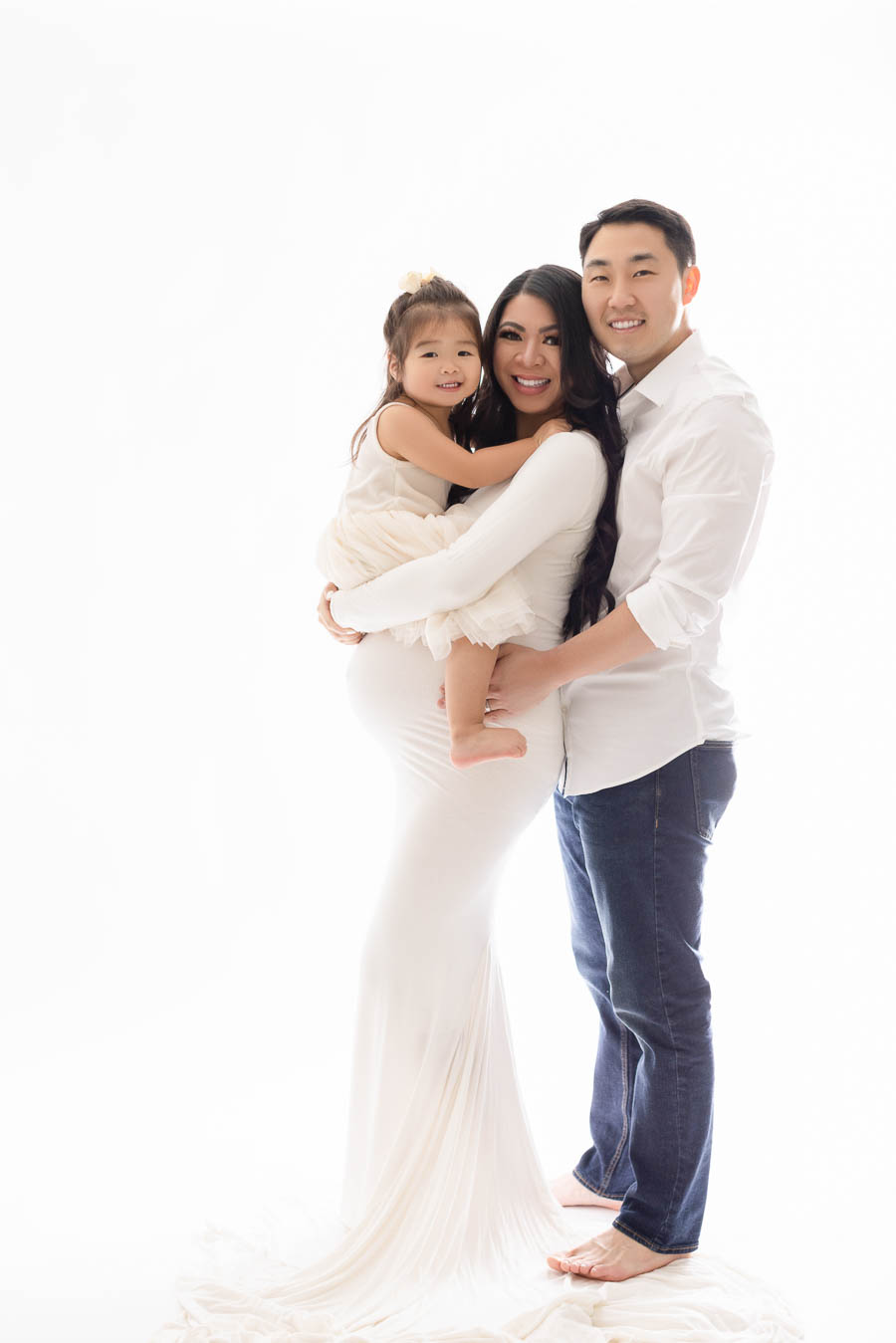 studio mommy and me maternity photo shoot with toddler girl, mom, and dad, white background and white dresses
