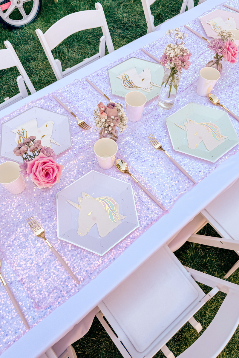 Unicorn tablescape for kids with iridescent tablecloth, pastel paper plates, unicorn-shaped napkins, and pink and gold plastic utensils